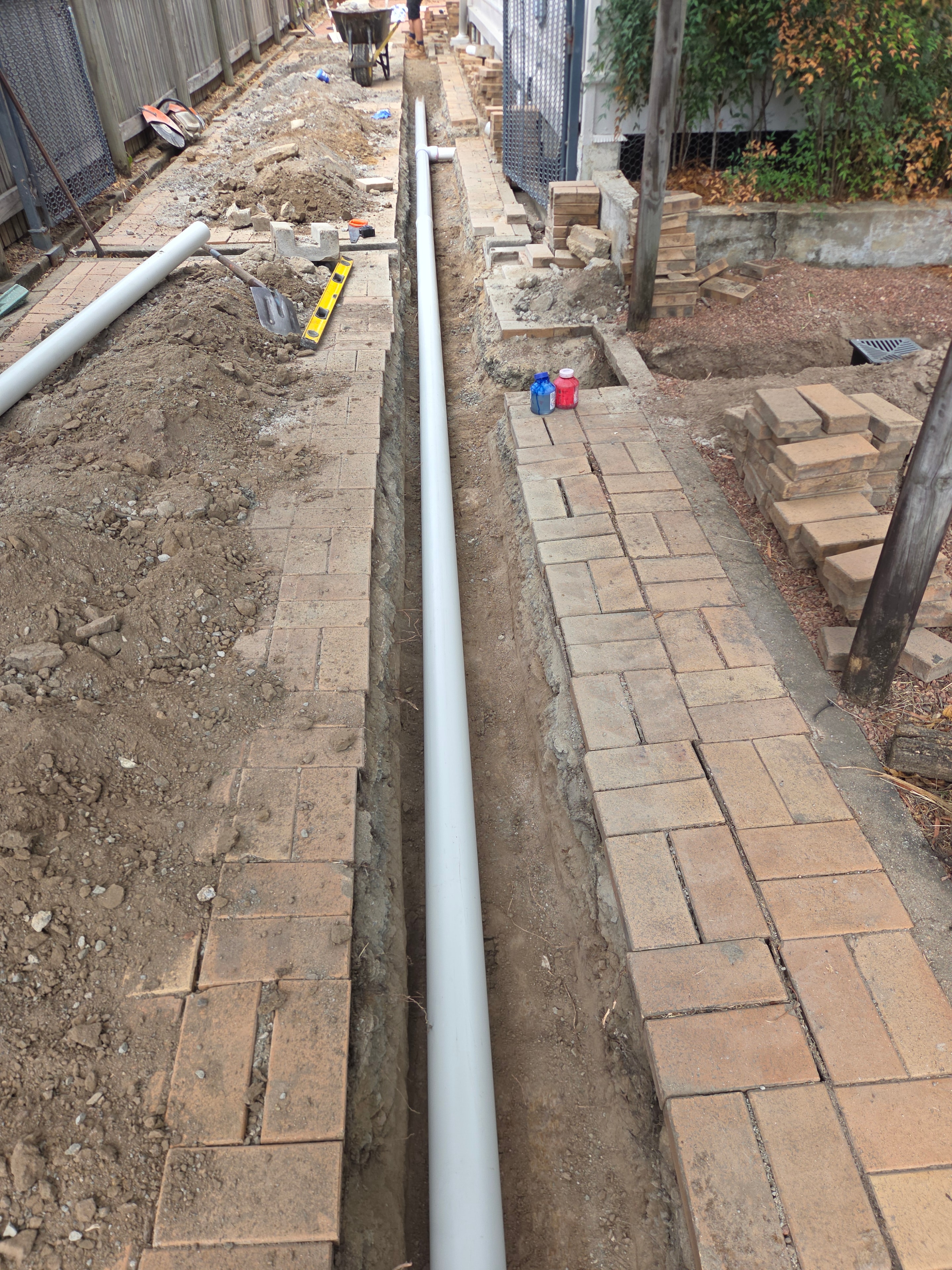 Drainage pipe run alongside brick paving — trench excavation and pipe laying