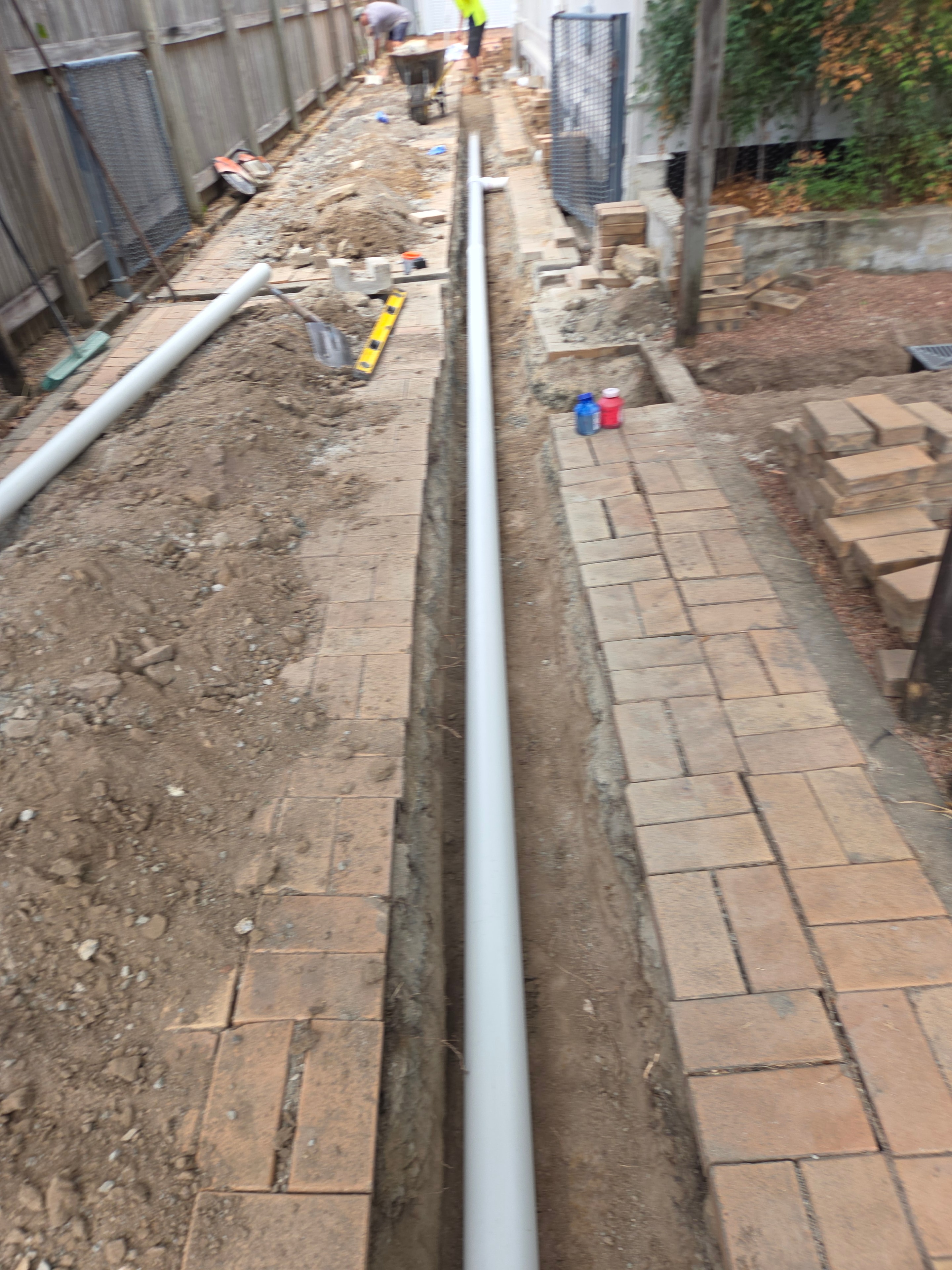 Drainage pipe installation in progress alongside brick retaining wall